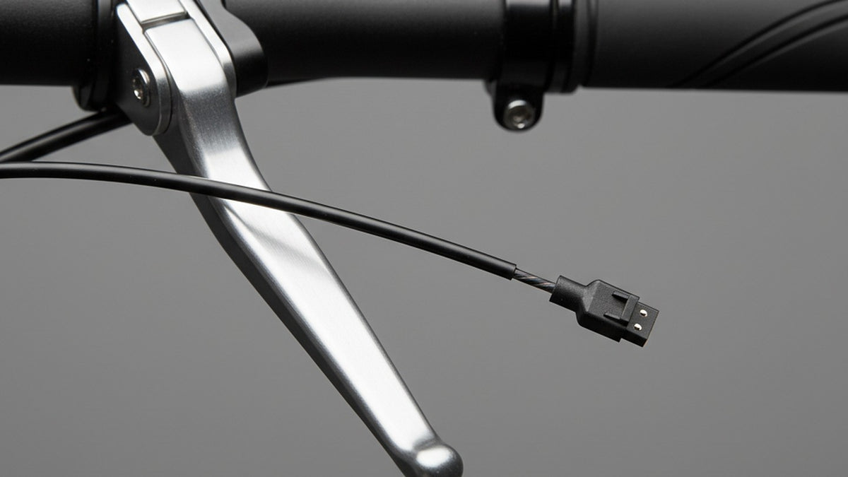 A close-up of an aluminium brake lever clamped on a black handlebar, with the brake cable and a thin sensor wire ending in a small two-pin connector, against a plain grey background.